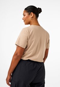 Camiseta de algodón beige de manga corta y cuello redondo, combinada con pantalones cargo negros de cintura elástica. Diseño limpio y sencillo.