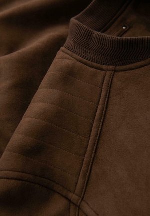 Brauner Pullover mit geripptem Kragen und strukturierten Nähten an der Schulter. Weiches Material mit einheitlicher Oberfläche und subtiler Schimmer.