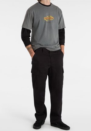 Grå T-shirt med et farverigt logo, lagd over en sort langærmet skjorte, parret med sorte cargo bukser og sorte sneakers.