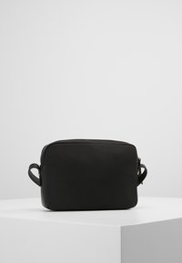 Borsa rettangolare nera realizzata in materiale liscio, con chiusura a zip e due manici ad anello sui lati, design minimalista.