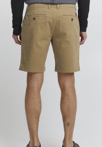 Shorts en khaki en coton avec une coupe droite, deux poches arrière avec fermetures à bouton et coutures visibles.