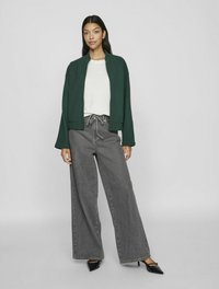 Grön avkortad jacka, vit texturerad tröja, grå högmidjade vida jeans och svarta spetsiga klackar. Enkel design, inga mönster.