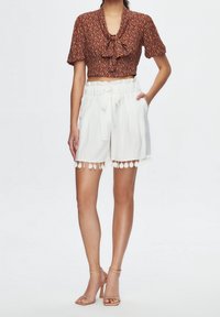 Brown patterned cropped blouse with a tie detail, paired with white shorts featuring a cinched waist and pom-pom trim at the hem.