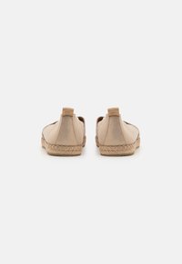 Un par de zapatos de espadrilles de ante beige con suelas de yute trenzado vistos desde la parte trasera sobre un fondo blanco.