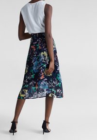 Blommig midikjol i marinblå, med ett livligt mönster med gröna, orange och blå accenter. I kombination med en vit ärmlös topp och svarta klackskor.