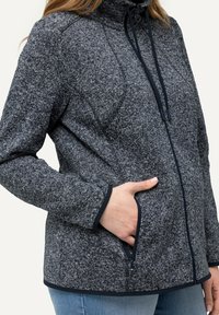 Torr texurerad, marinblå fleecejacka med hög krage, framdragkedja och sidofickor. Har kontrasterande mörka kanter längs sidorna.