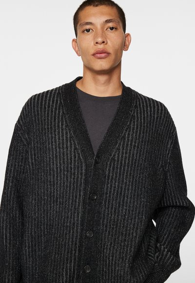 Sort strikket cardigan med lodret ribbet tekstur, dyb v-udskæring, seks knapper foran og drop shoulders for en afslappet pasform.