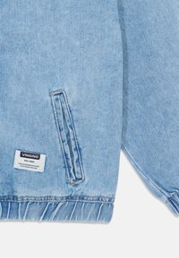 Veste en denim bleu clair avec une poche frontale à ouverture cousue, ourlet effiloché et une étiquette affichant la marque "VINGINO."