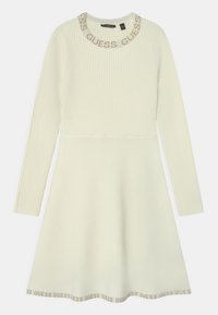 Abito a maniche lunghe in maglia di un crema chiaro, con una texture a costine, scollatura rotonda con il marchio "GUESS" e gonna svasata.
