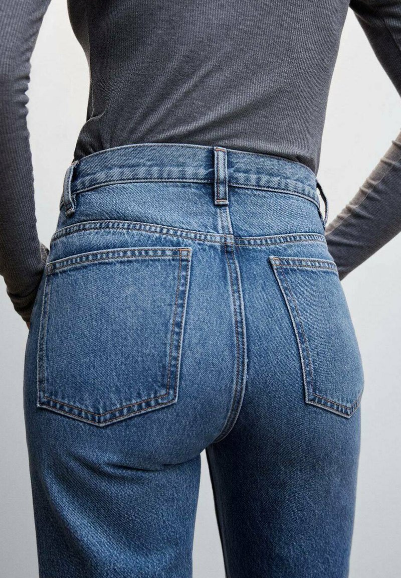 Jeans en denim bleu taille haute avec deux poches arrière, texture décolorée et couture contrastante. Associés à un haut ajusté à manches longues.