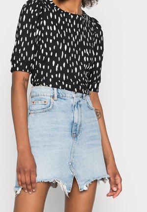 Top negro con un patrón de lunares blancos, con mangas cortas. Combinado con una falda de mezclilla azul clara, con dobladillo deshilachado y detalle de abertura frontal.