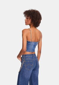 Top corto in denim con spalline a catena, colore azzurro chiaro, design aderente. Abbinato a jeans a gamba larga con dettagli in catena e tasche posteriori.