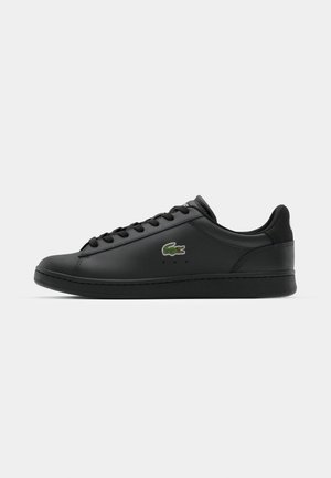 Zapatilla de cuero negra con una textura suave, punta redonda, cordones tonales y un logo bordado en verde en el lateral. Suela de goma de perfil bajo.