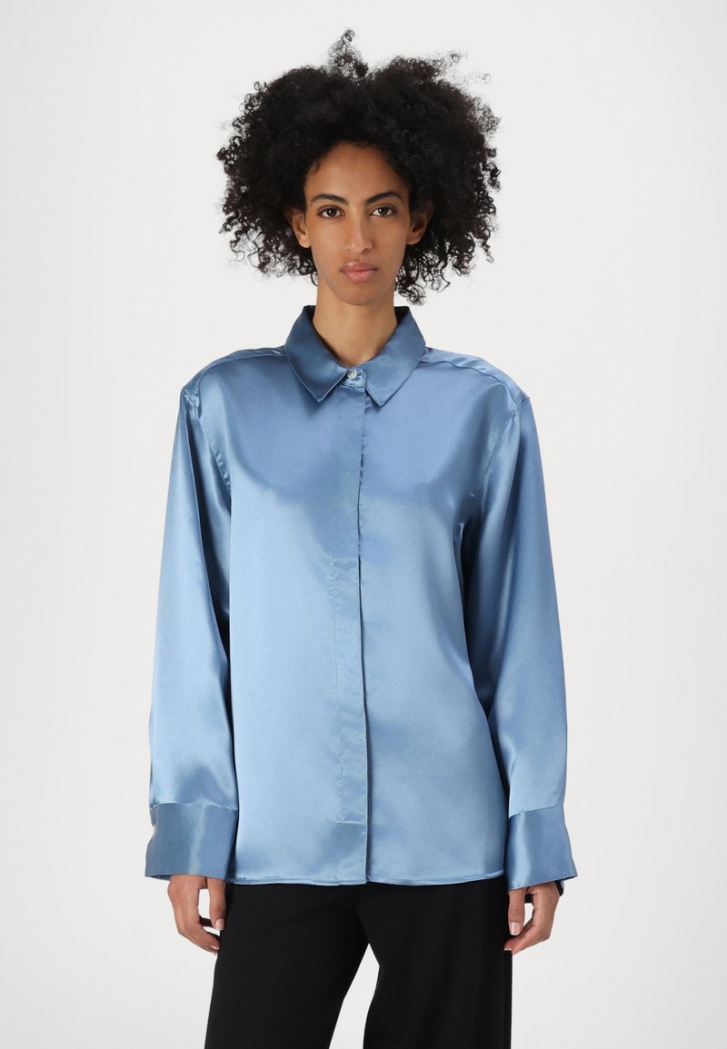 Camicia blu satin con bottoni, colletto, maniche lunghe e polsini. Tessuto liscio e vestibilità sagomata con un leggero lucido.