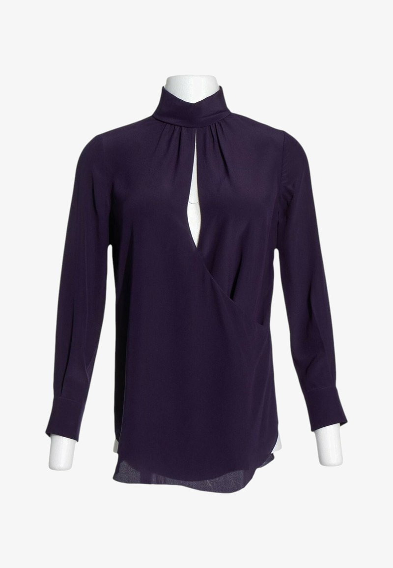Blouse à manches longues violet foncé avec col montant et ouverture en forme de serrure à l'avant sur un buste de mannequin blanc.