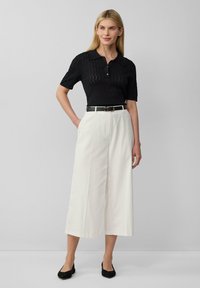 Zwart poloshirt met korte mouwen en een gestructureerd design, gecombineerd met witte wijde broek, verfraaid met een zwarte riem en zwarte flats.