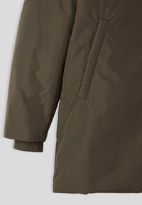 Giacca imbottita verde oliva con texture liscia, tasca laterale e polsini a costine. Il design è casual con una silhouette dritta.