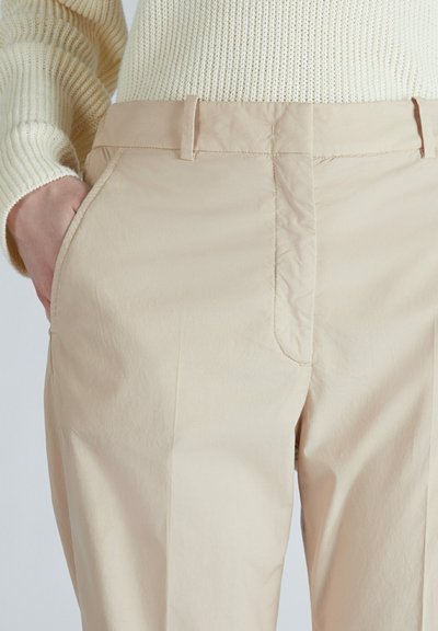 Un pantalon beige en tissu lisse et léger avec une coupe ajustée. Comprend des poches avant et des détails de couture subtils sur les coutures.