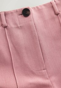 Roosa tekstuuriga kangast püksid, millel on küljetasku ja must nööp sulgemiseks vöökohal, triipude detailidega kujunduse rõhutamiseks.