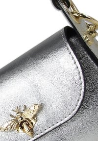 Sac à main en métal argenté avec un accent doré en forme d'abeille et des détails de couture sur les bords. Comprend un fermoir et une attache chaîne.