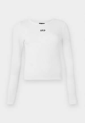 Hvit langermet ribbestrikket topp med rund hals og liten svart "GAP" logo i midten. Myk, strammende stoff med en tettsittende design.