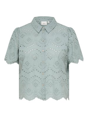 Blouse vert clair à manches courtes, boutonnée, avec bords festonnés et broderie ajourée élaborée aux motifs floraux et circulaires.