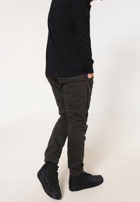 Mörk olivgrön cargobyxor med sidofickor, kombinerat med svarta högstövlar och en svart långärmad tröja.