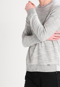 Suéter gris de manga larga con un patrón texturizado, cuello redondo y dobladillo en contraste. Fabricado con una tela suave y de corte relajado.