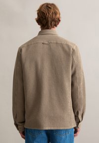 Beige geweven shirt met een gestructureerd patroon, knoopmanchetten en een kraag, gecombineerd met blauwe spijkerbroek. Zichtbare naden en een comfortabele pasvorm.