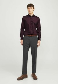 Bordeauxkleurig overhemd met lange mouwen en een button-down kraag, gecombineerd met grijze op maat gemaakte broek en bruin leren schoenen. Een bruine riem maakt de look af.