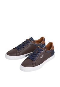 Barna sportcipő tengerészkék fűzőkkel, világosbarna díszítésekkel, sima felülettel, fehér gumitalppal, oldalon logóval és kényelmes párnázott szegéllyel.