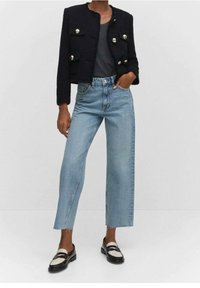 Veste courte marine à boutons argentés, associée à un jean bleu clair à jambes larges et des chaussures noires avec des brides blanches et noires.