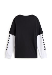 Czarny krótki T-shirt noszony na białych długich rękawach z czarnym wzorem kwadratów wzdłuż zewnętrznych ramion, widziany od tyłu.