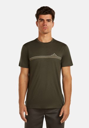 Hombre que lleva una camiseta de manga corta color verde oliva con una línea horizontal blanca y un diseño de montaña a lo largo del pecho.