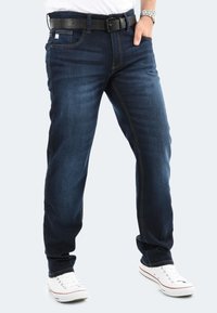 Dark blue denim jeans with a straight fit, featuring contrast stitching and a black belt. Paired with white sneakers.