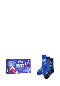 Tři páry ponožek v dárkové krabičce. Ponožky mají zimní motivy, modré, tmavě modré a pruhované vzory se vzory lyžařů a sněhových vloček. Krabička je modrá s bílými stromy a domy.