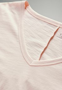 Jasnoróżowa bawełniana koszulka z dekoltem w kształcie V o miękkiej fakturze, z przeszytym dekoltem i luźnym krojem, ułożona na płasko do ekspozycji.