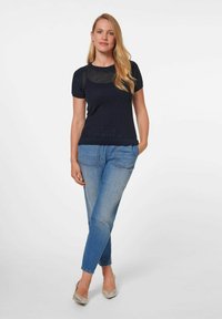 Marineblaues, gestricktes Kurzarmoberteil mit einem strukturierten Muster, kombiniert mit ausgewaschenen blauen Jeans und hellsilbernen, spitzen Absatzschuhen.