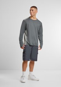 Langermet grå treningsskjorte med lomme og mesh-sidestykker, satt sammen med mørkegrå cargo-shorts med sidelommer.
