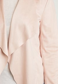 Ljusrosa, mjuk tygblazer med draperad front, som har en slät ytstruktur och inga synliga knäppningar eller fickor.