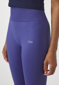 Lilla aktivtøy leggings laget av elastisk stoff, med en ribbet høy livlinje, logo detaljer og teksturerte sideakenter.