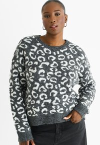 Grauer Pullover mit weißem Leopardenmuster, Rundhalsausschnitt, strukturiertem Stoff und gerippten Bündchen und Saum. Kombiniert mit schwarzen Jeans.