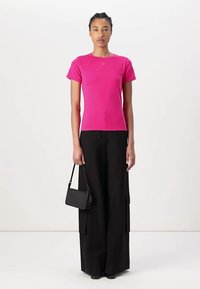 T-shirt ajusté à manches courtes fuchsia avec un col rond, associé à un pantalon large noir taille haute et un petit sac à main noir.