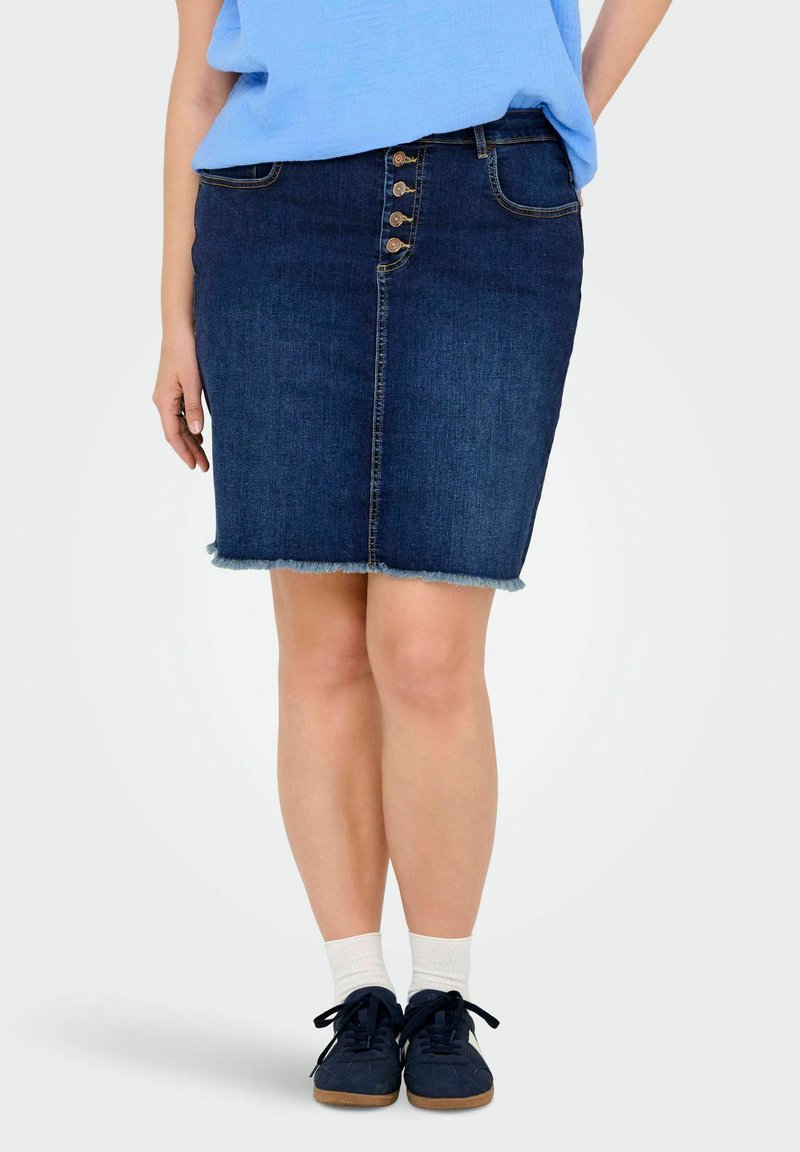 Jeans krilo s prilagojeno silhueto, temno modre barve, sprednjim gumbom za zapiranje in strganim robom. Nosimo ga z mornarskimi čevlji in belimi nogavicami.