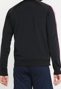 Schwarze Sportjacke mit glatter Textur, ausgestattet mit pinken Seitenstreifen und einem gerippten Taillenbund. Entworfen mit langen Ärmeln und einem hohen Kragen.