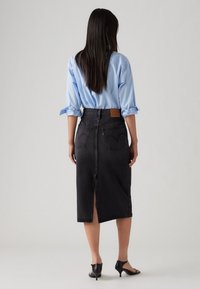 Musta denim-midi-hame, jossa on takaröyhelö ja kaksi takataskua. Yhdistetty vaaleansiniseen napilliseen paitaan ja mustiin korkokenkiin.
