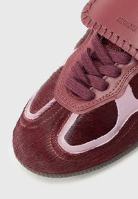 Burgundy sneaker featuring a hair-on-hide texture, leather accents, a padded tongue, and dark laces, with a rubber sole and cutout design.