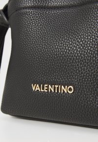Borsa in pelle nera con texture, caratterizzata da un logo "VALENTINO" in oro a rilievo sul davanti. Finitura liscia con una forma strutturata.