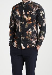 Zwart shirt met lange mouwen en bloempatroon, versierd met kleurrijke bloemen in wit-, oranje- en groentinten, voorzien van een boord met knopen en een aansluitend model.