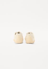 Beige athletic shoes with a textured rubber sole, padded collar, and branding at the heel. Designed for comfort and support.